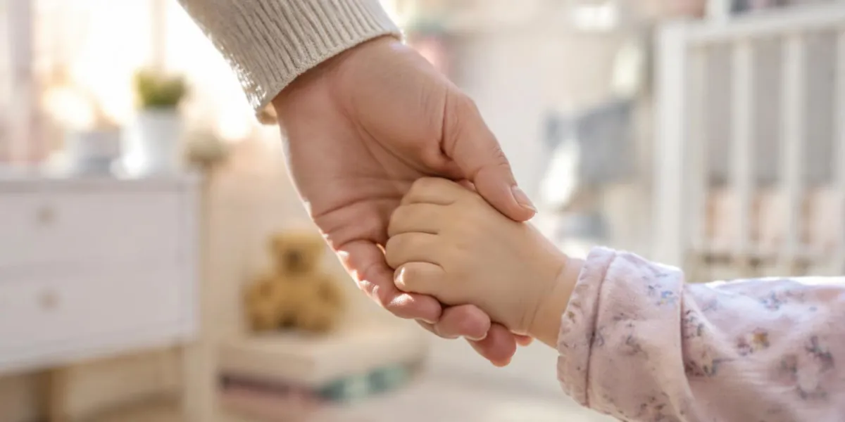 An adult's hand gently holding a toddler's small hand
